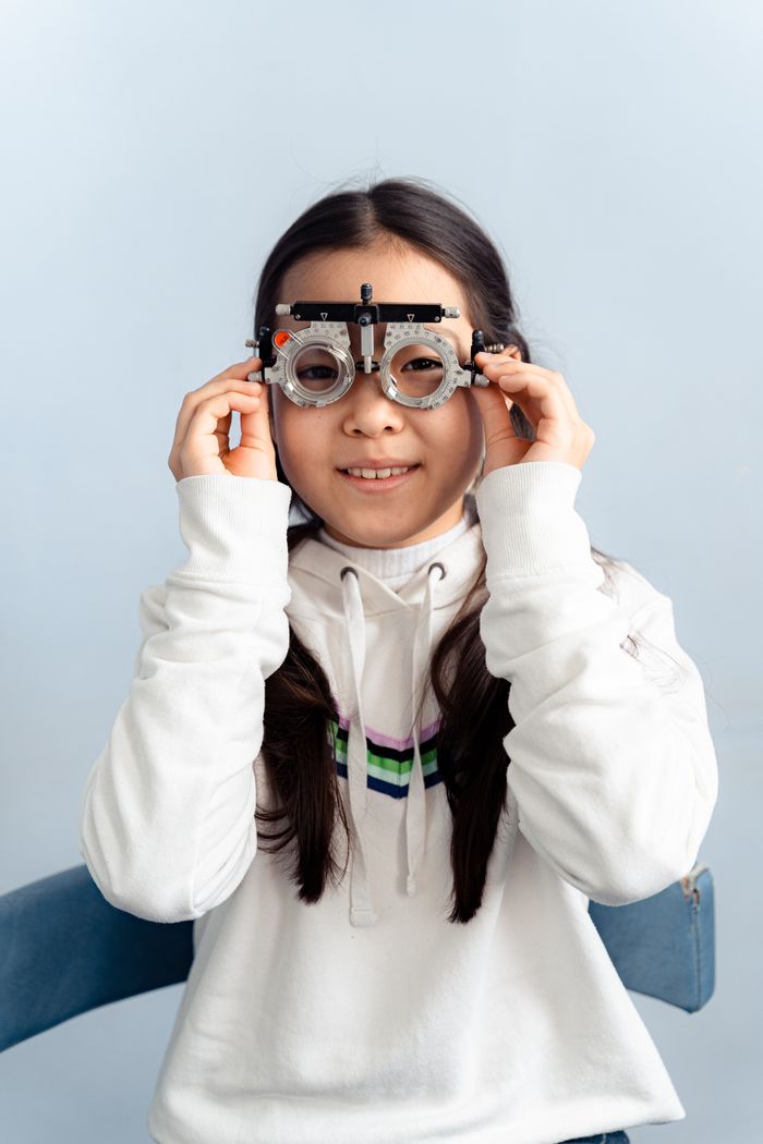 Teen girl wearing optometry test glasses indoors, checking vision with a smile.